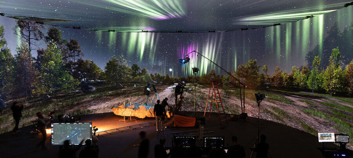 A virtual production stage features large LED screens with a nighttime forest scene. Performers and filmmakers are at work in front of it.