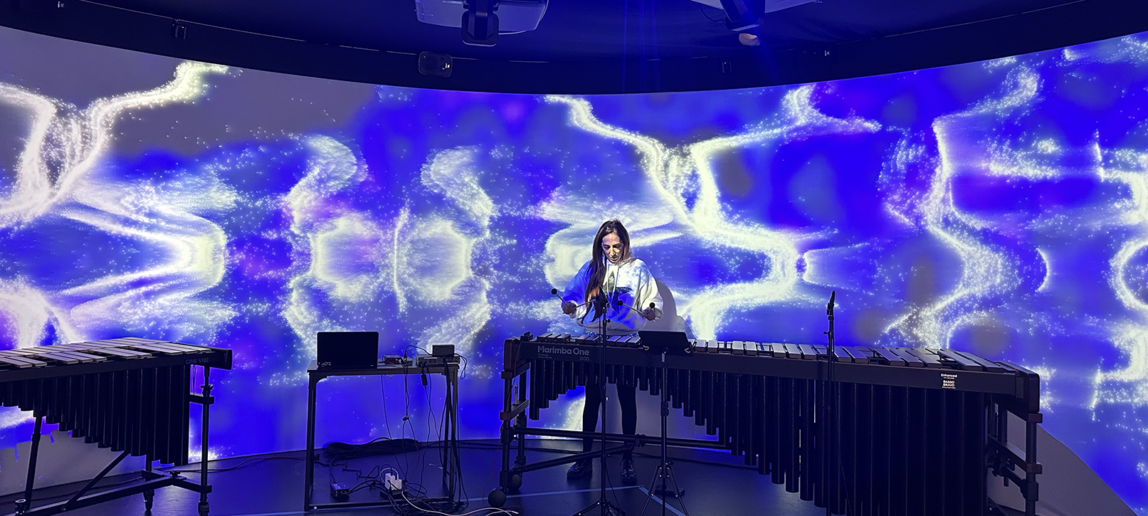 A musician plays the marimba in front of a 360-degree screen showing blue and white patterns and designs.