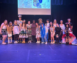 A college professor stands with her students, who are all dressed in outfits made with recyclable materials.