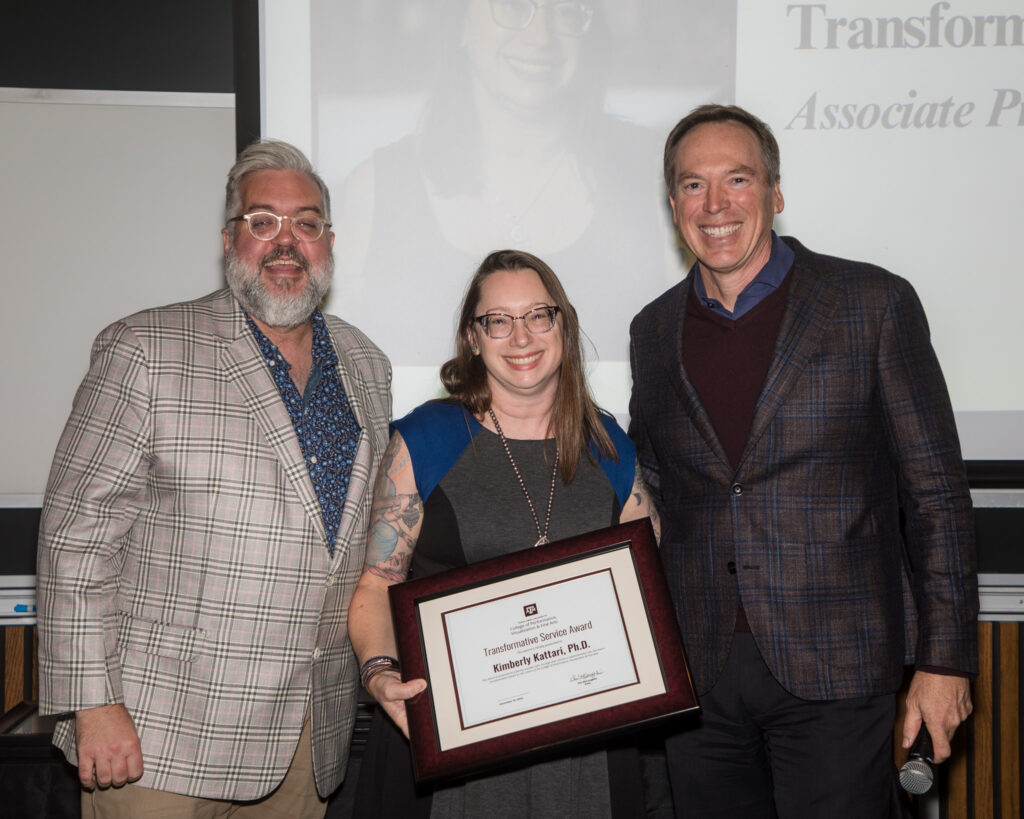 A woman holds a framed certificate of achievement. Two university leaders stand alongside her.