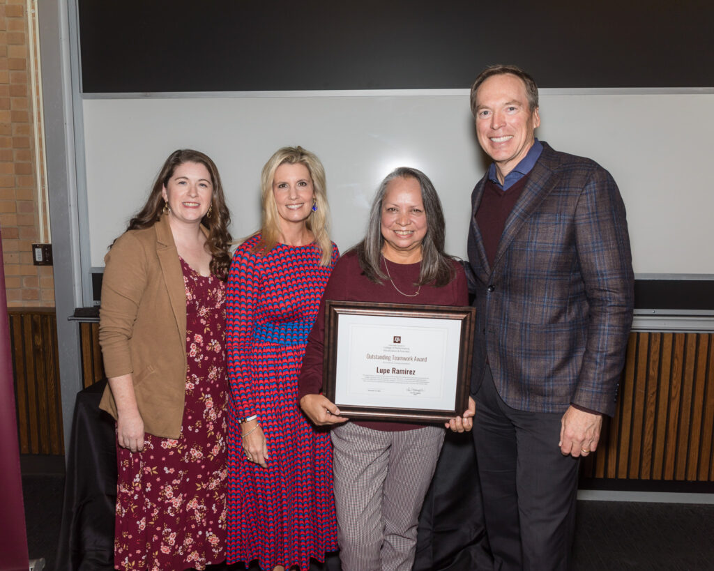 A smiling woman holds a framed certificate of achievement. Around her are three university leaders.