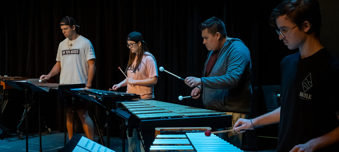 Three college students and a professor play marimba in a black box theater.