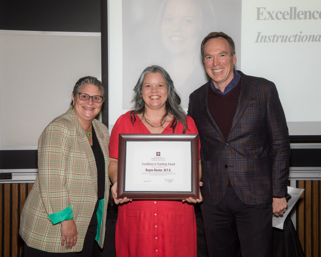 A smiling woman holds a framed certificate of achievement. A university dean is pictured on her left, an associate dean on her right.