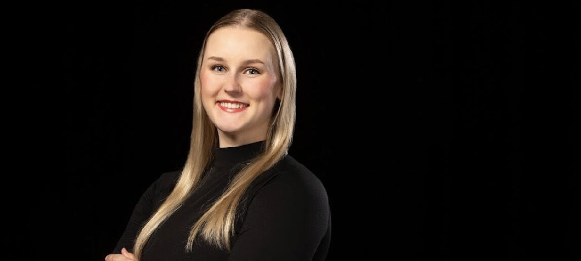 A college student smiles in front of a black background.