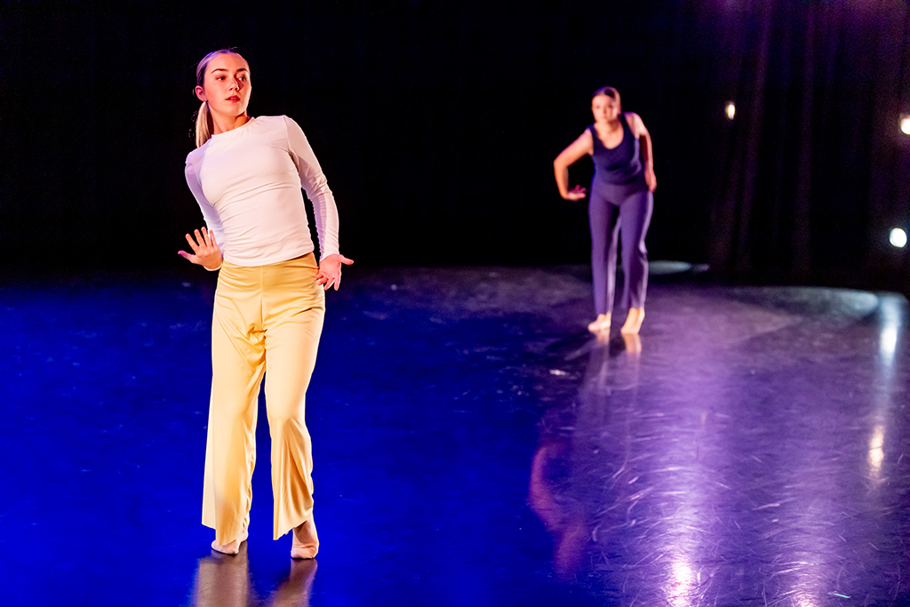 Two college students dance on a stage, with a blue light shining on them.