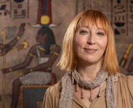 An Egyptologist stands in front of a display of ancient markings.