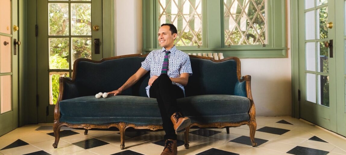 A percussion performer sits on a couch with marimba mallets at his side.