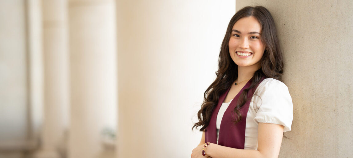 A college student wearing a maroon Texas A&M graduation sash smiles for a portrait.