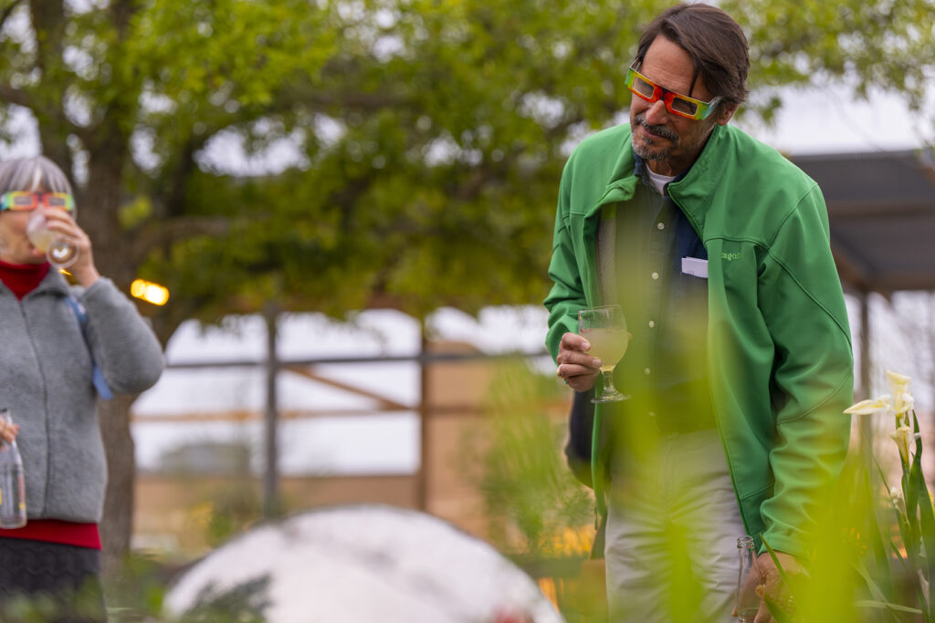A man wearing kaleidoscopic glasses cocks his head as he views something in an outdoor setting.